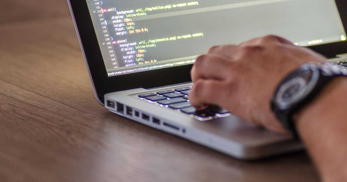 A hand typing on a laptop that shows code